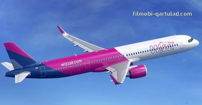 Side profile of a Wizz Air Airbus plane in flight against a bright blue sky with light clouds, showing the distinctive purple and pink livery and logo.